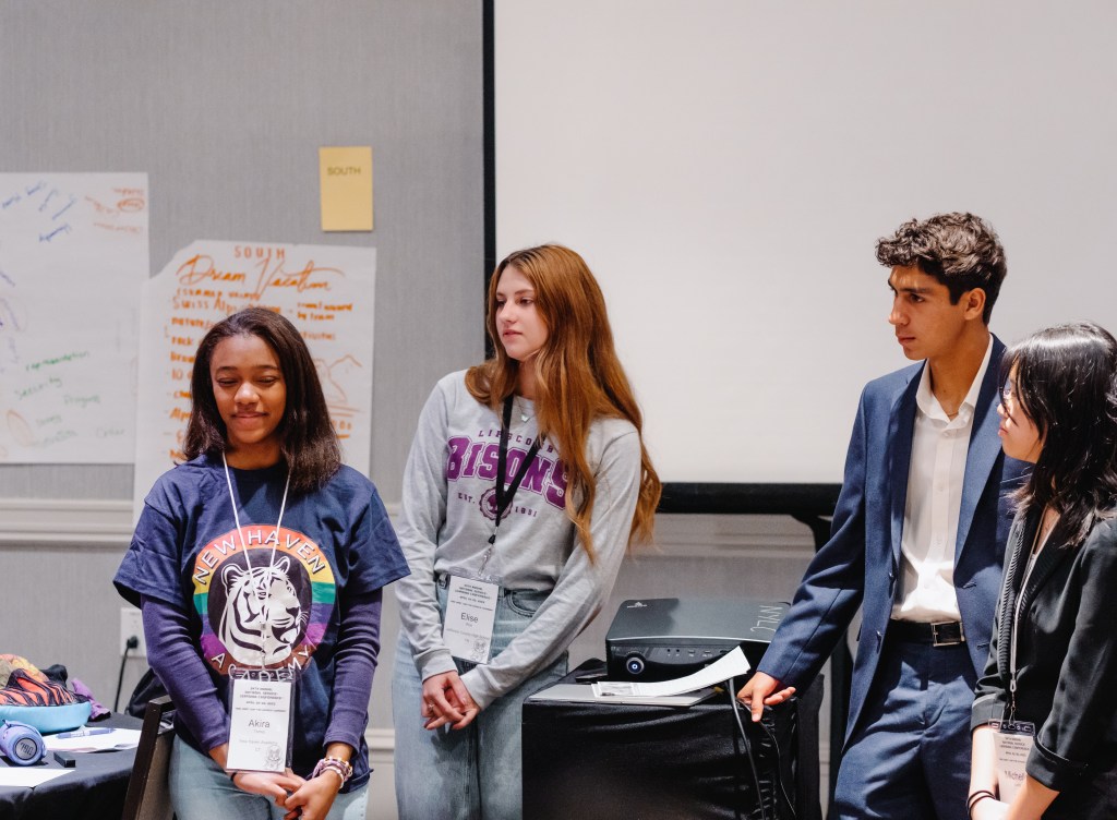 High school students listen in as a middle school student shows off her service-learning project